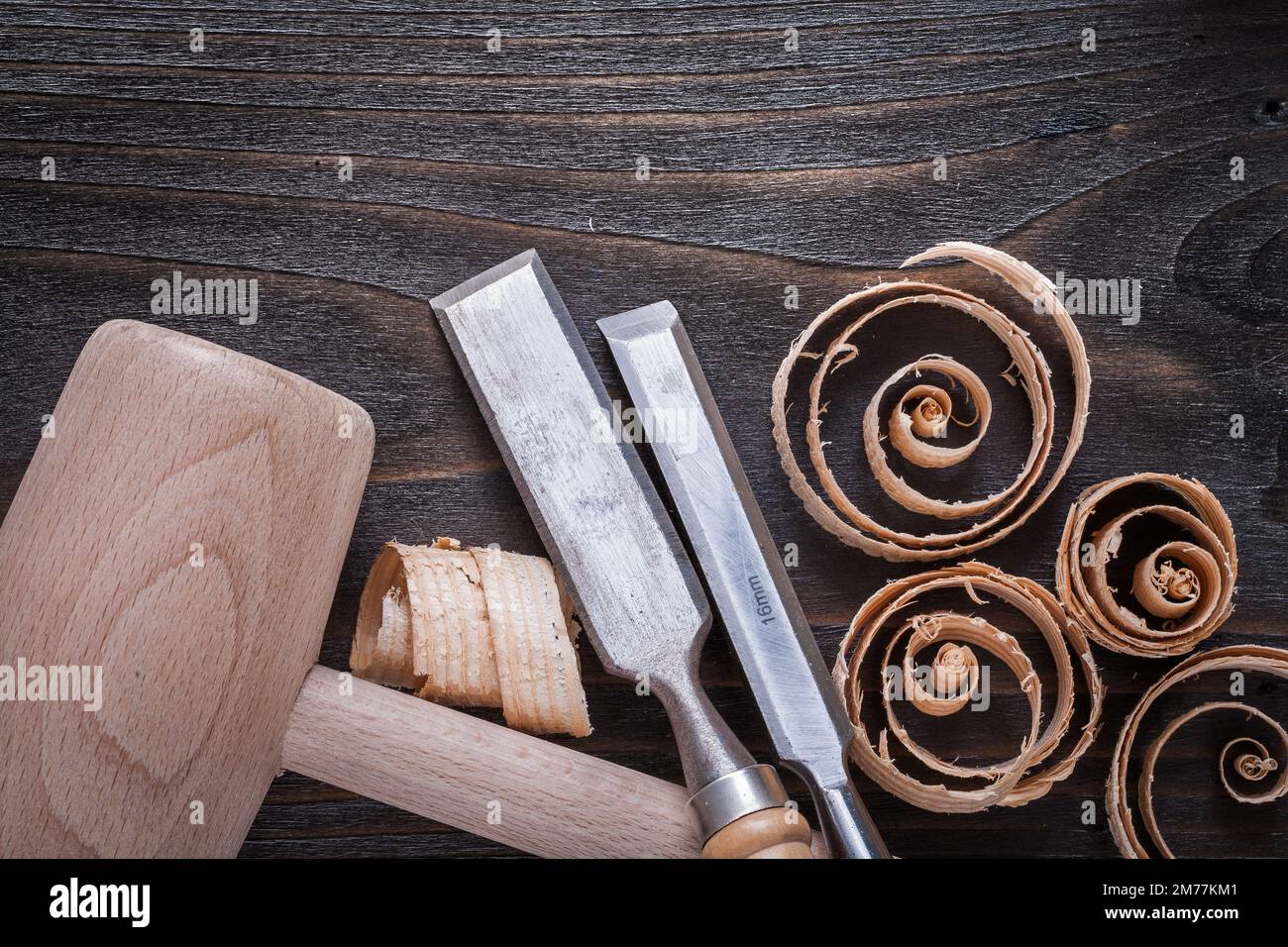 Wooden mallet chisels and curled up planing chips on vintage wood board construction concept. Stock Photo