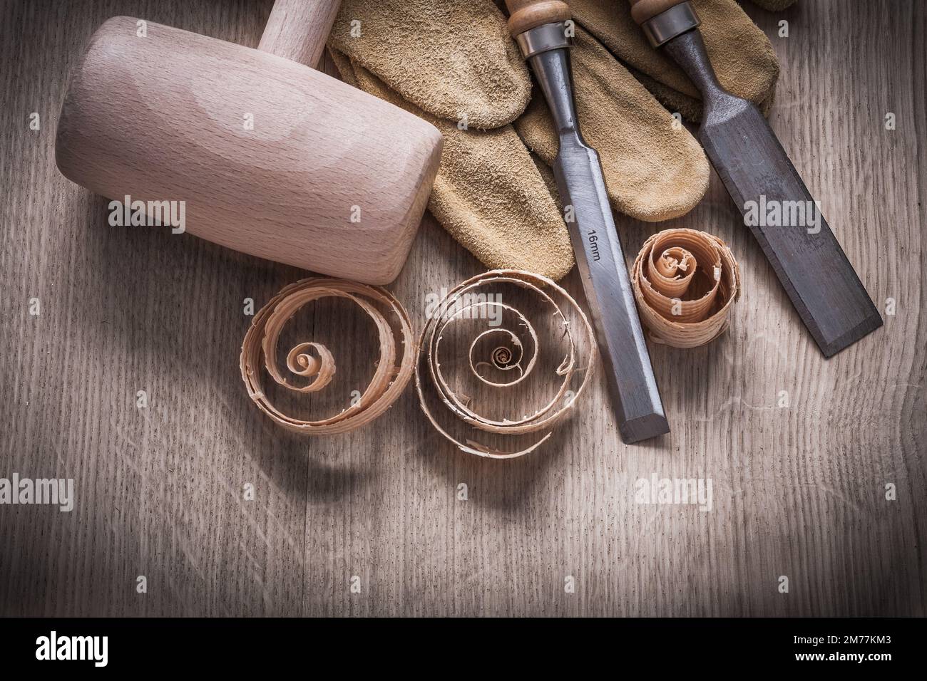 Wooden mallet curled up shavings firmer chisels leather gloves on wood board construction concept. Stock Photo