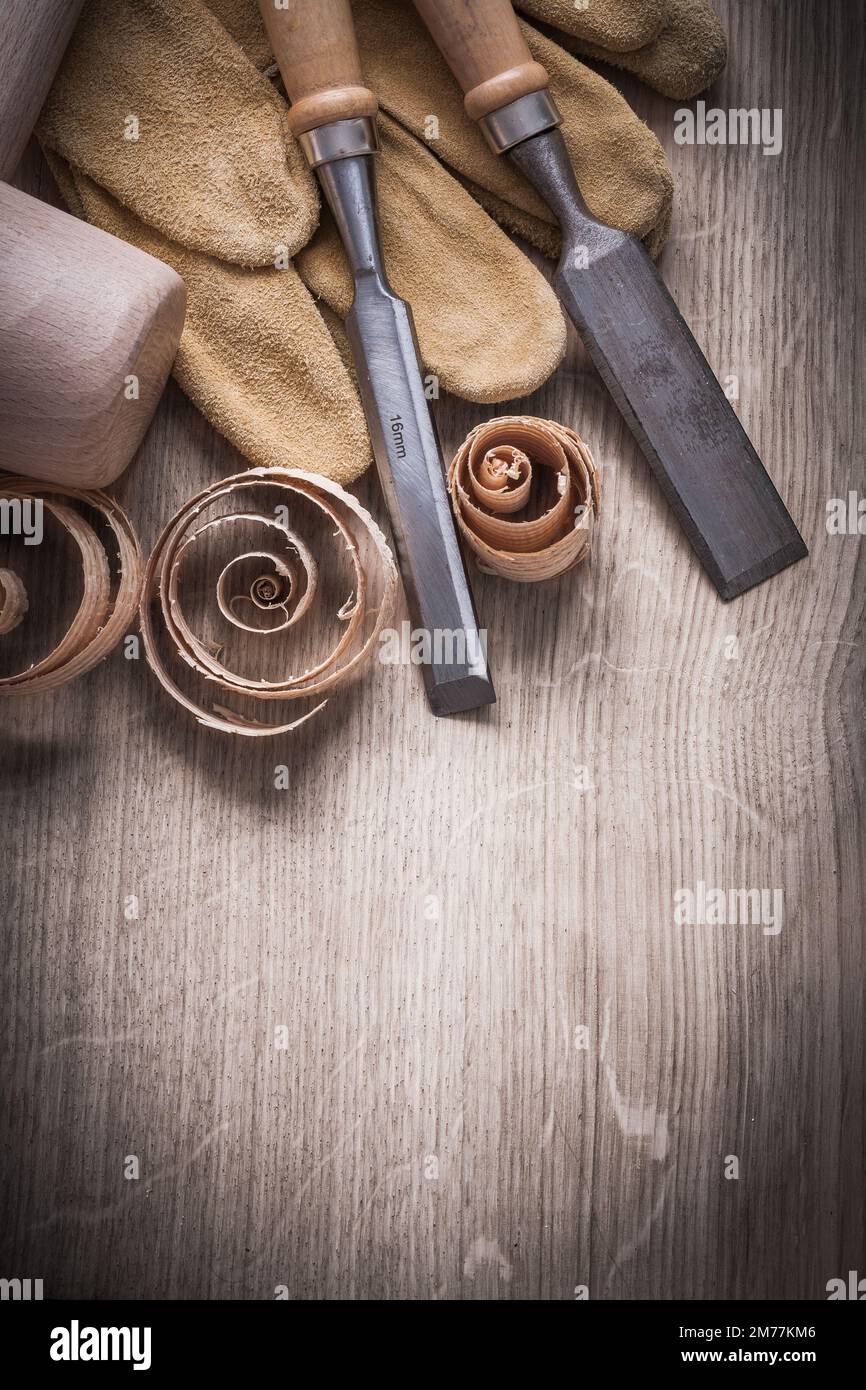 Wooden mallet curled up shavings flat chisels leather gloves on wood board vertical view construction concept. Stock Photo