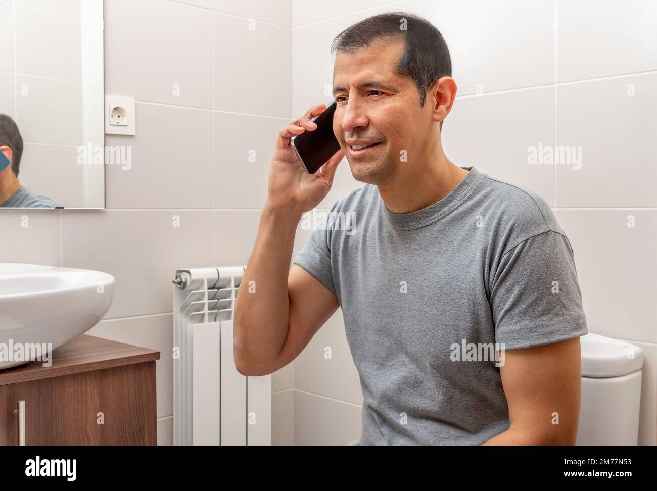 Shot of a man using a phone while sitting on the toilet in a bathroom Stock Photo