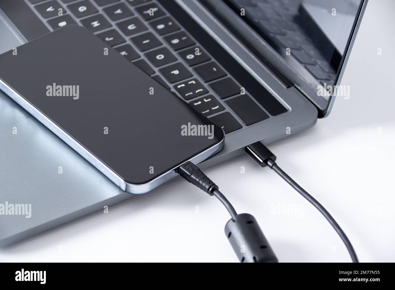 Connect smartphone to laptop for data dump via USB cable on white table