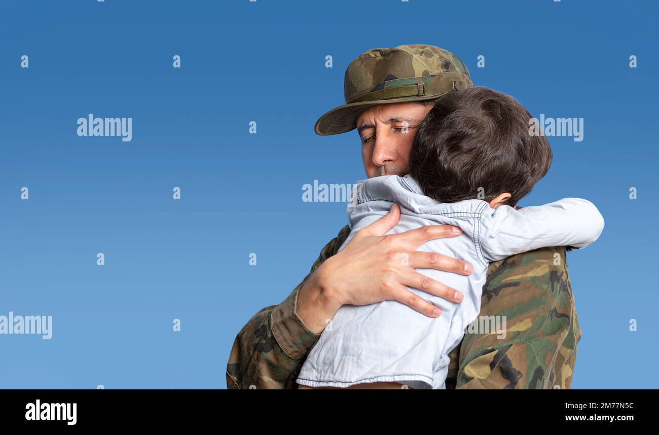 Military father hugs his son when they are reunited after a mission with a blue sky in the background and copy space. Stock Photo