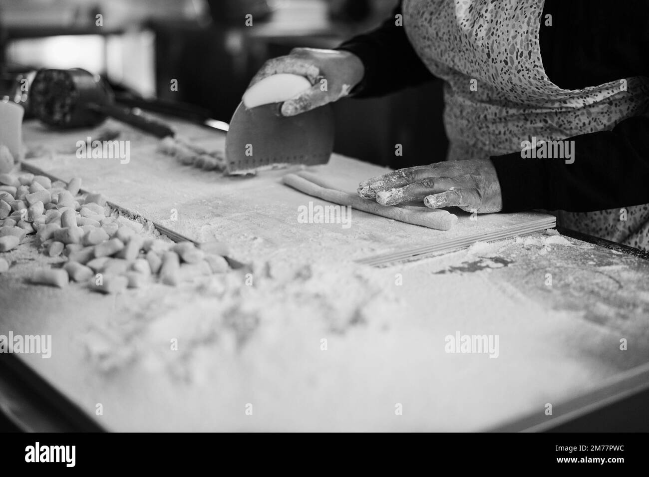 Woman preparing dough for gnocchi inside pasta factory - Soft focus on right hand - Black and white editing Stock Photo