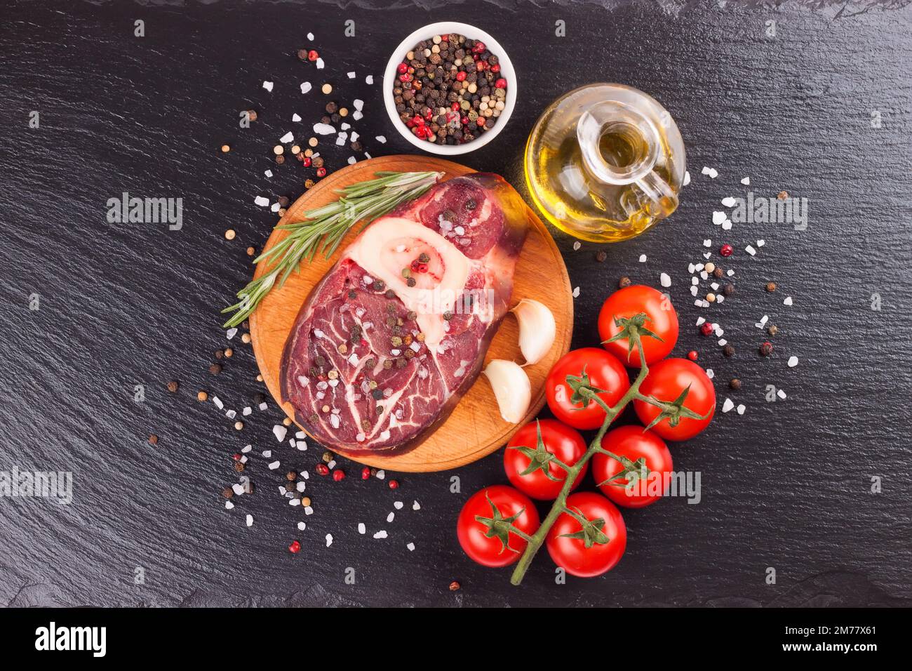 raw meat beef steak with bone, spices, rosemary and cooking ingredients on cutting board and black slate background. top view, flat lay. Stock Photo