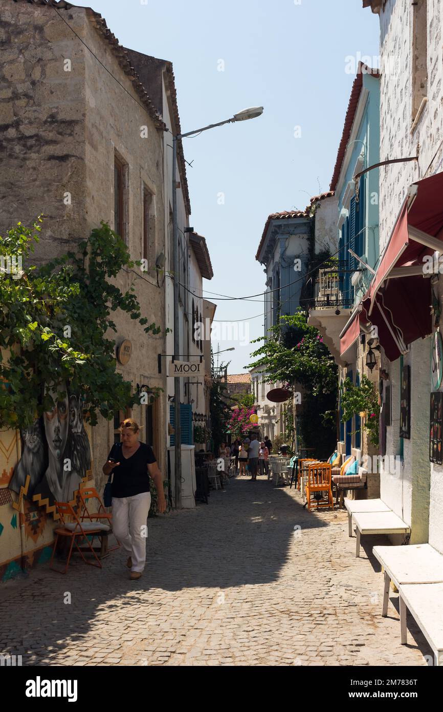 View of people walking on street and old, historical, traditional stone houses in famous, touristic Aegean town called Alacati. It is a village of Ces Stock Photo