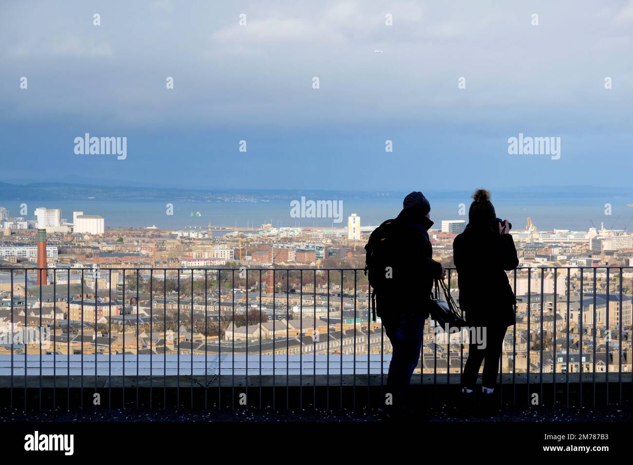 Edinburgh, Scotland, UK. 8th January 2023. Visitors on Calton hill wrapped up against the cold blustery wind and changeable weather conditions. View north over city rooftops towards the Forth estuary. Credit: Craig Brown/Alamy Live News Stock Photo