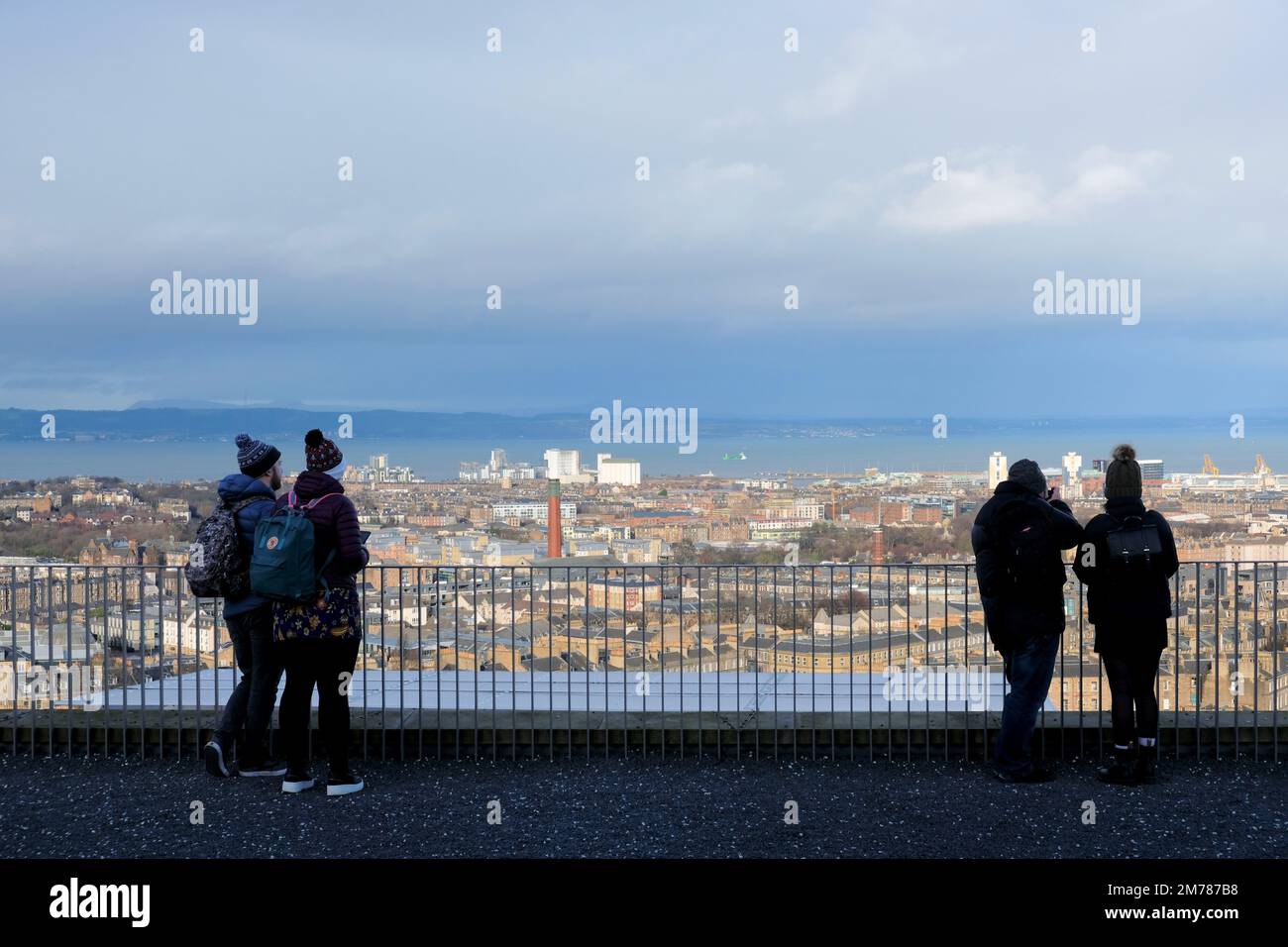 Edinburgh, Scotland, UK. 8th January 2023. Visitors on Calton hill wrapped up against the cold blustery wind and changeable weather conditions. View north over city rooftops towards the Forth estuary. Credit: Craig Brown/Alamy Live News Stock Photo