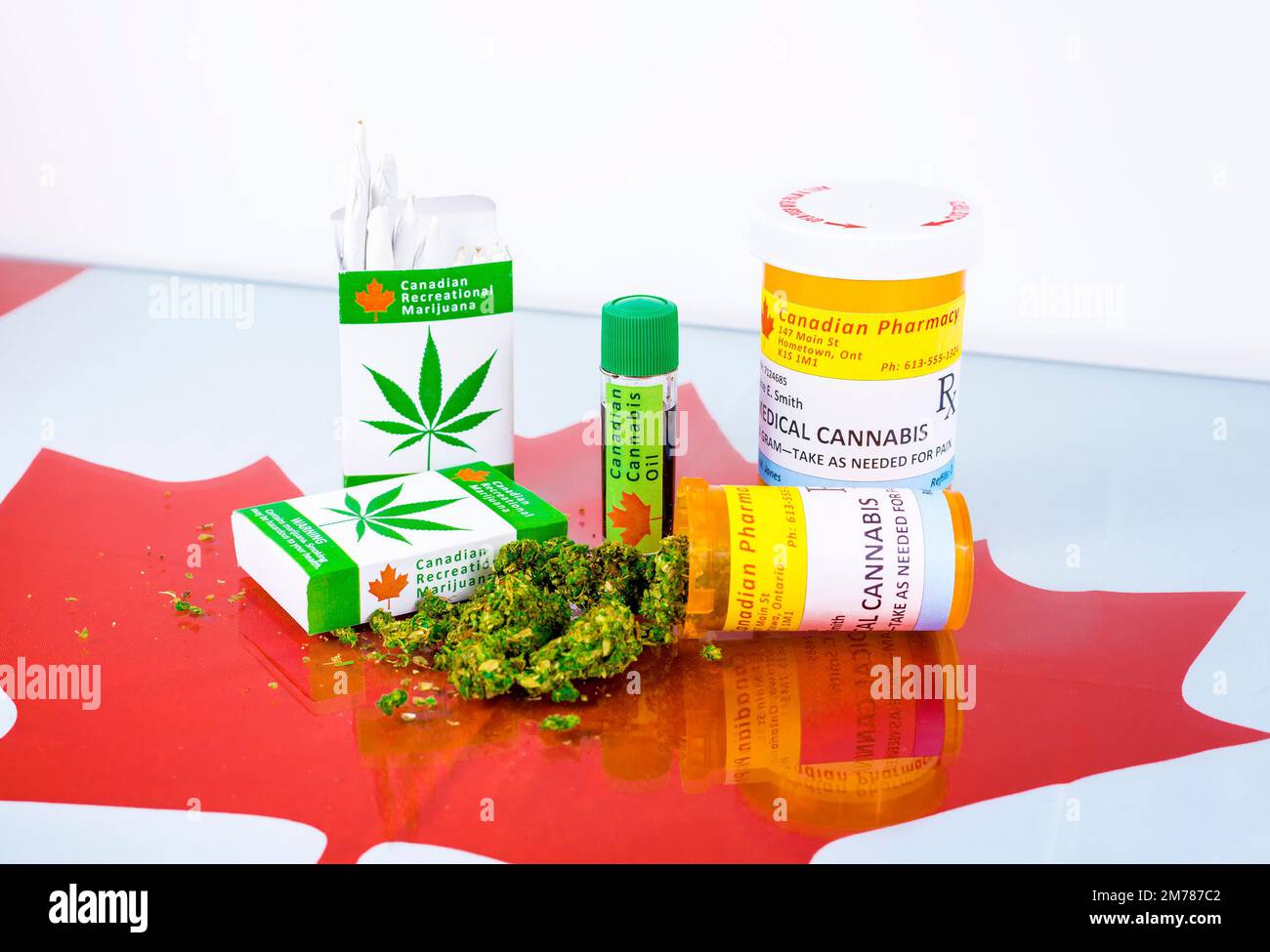 Cannabis in Canada. Marijuana cigarettes, cannabis oil, and prescription bottles for cannabis on a glass table. Buds spill from one of the bottles. Stock Photo