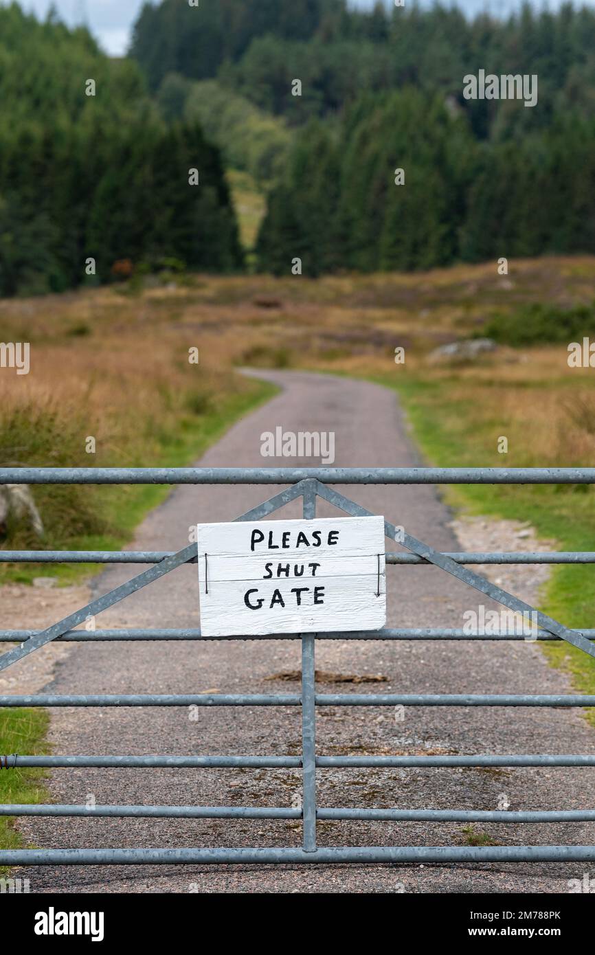 Narrow country lane with a gate on, sign on the gate saying 'Shut the gate' on it. Highlands of Scotland, UK. Stock Photo