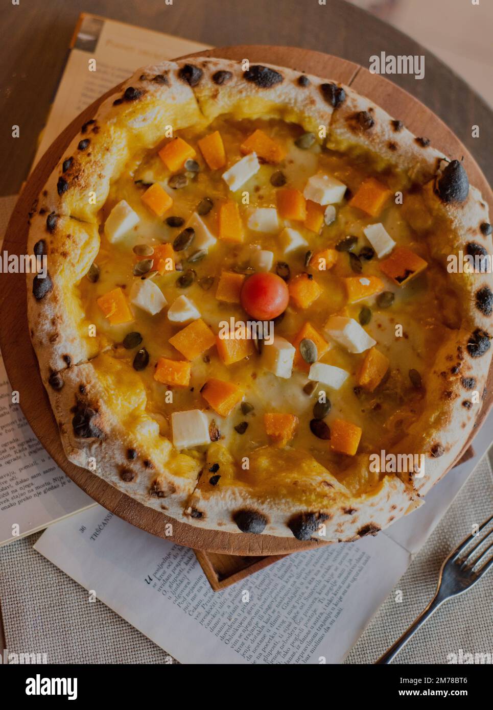 A top closeup of pizza with vegetables on a wooden board, newspapers around Stock Photo