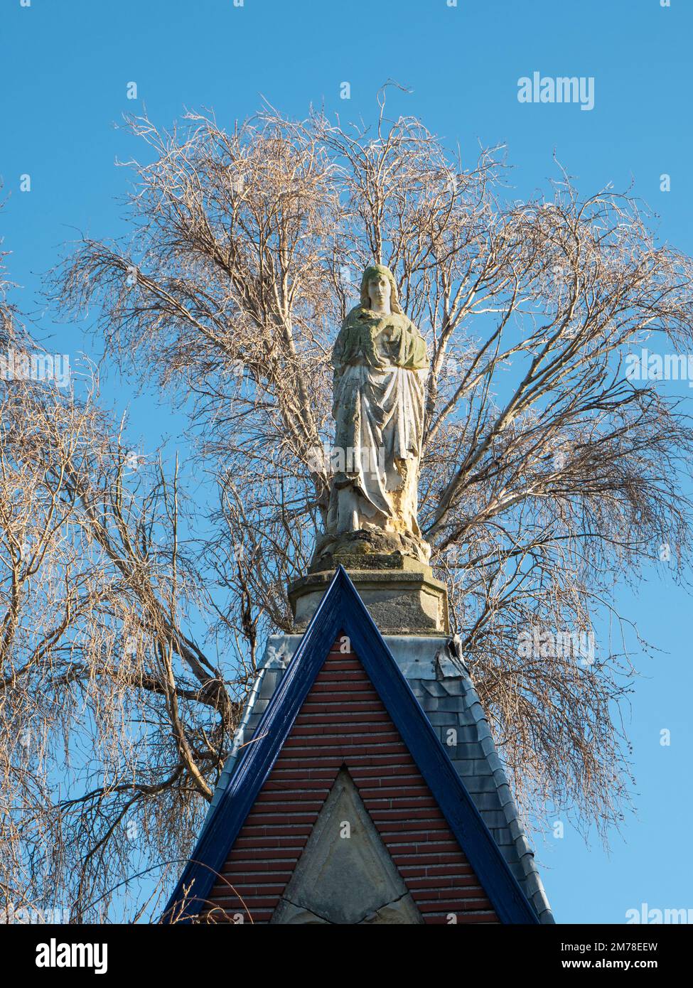Statue of the Virgin Mary with a dry tree in the background Stock Photo
