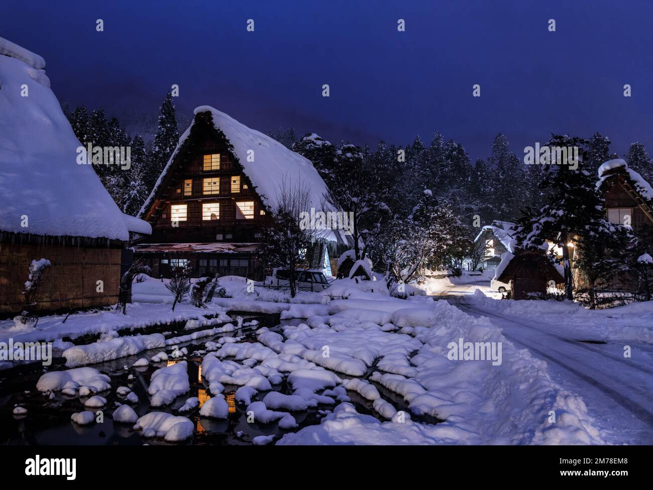 Snow covered Japanese farmhouse in historic village by woods at night  Stock Photo
