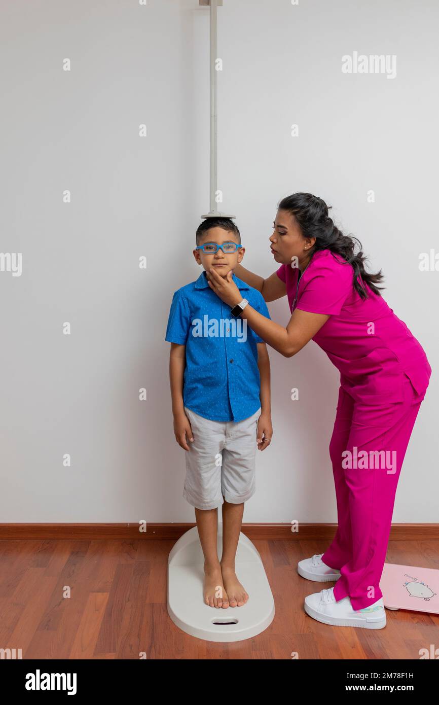 Latina pediatrician measuring a child with a wall ruler in her office. Stock Photo