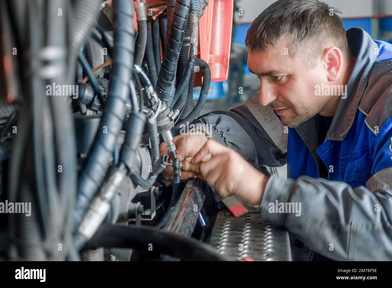 Car mechanic repairs large truck or tractor in workshop. Professional mechanic repairs truck engine. Genuine worker.. Stock Photo