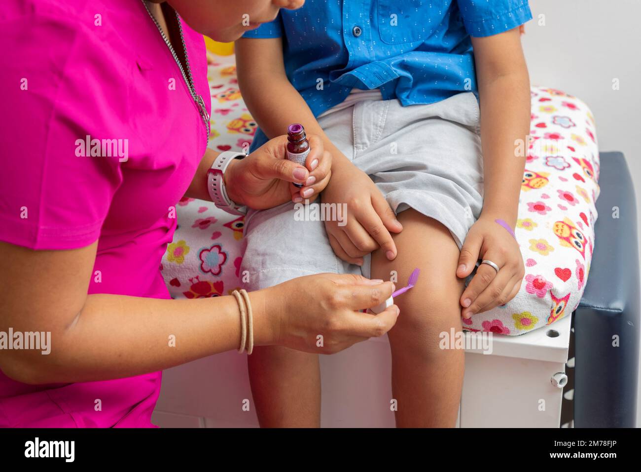Unrecognizable female doctor is treating a child's knee in her medical office. Stock Photo