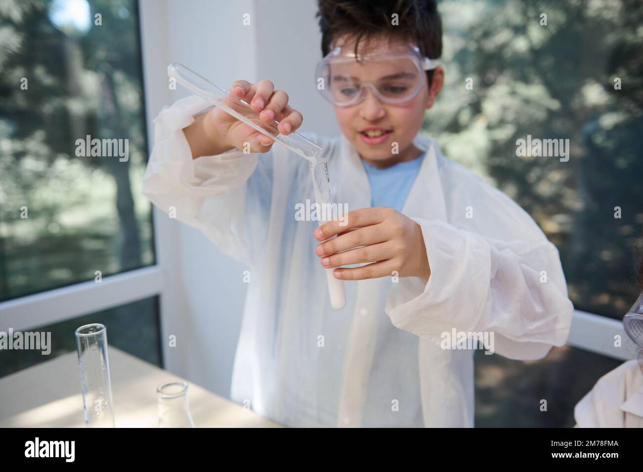Focus on hands of a smart schoolboy pours reagent into a test tube ...