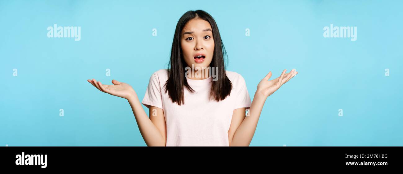 Confused asian girl spread empty hands sideways, shrugging shoulders ...