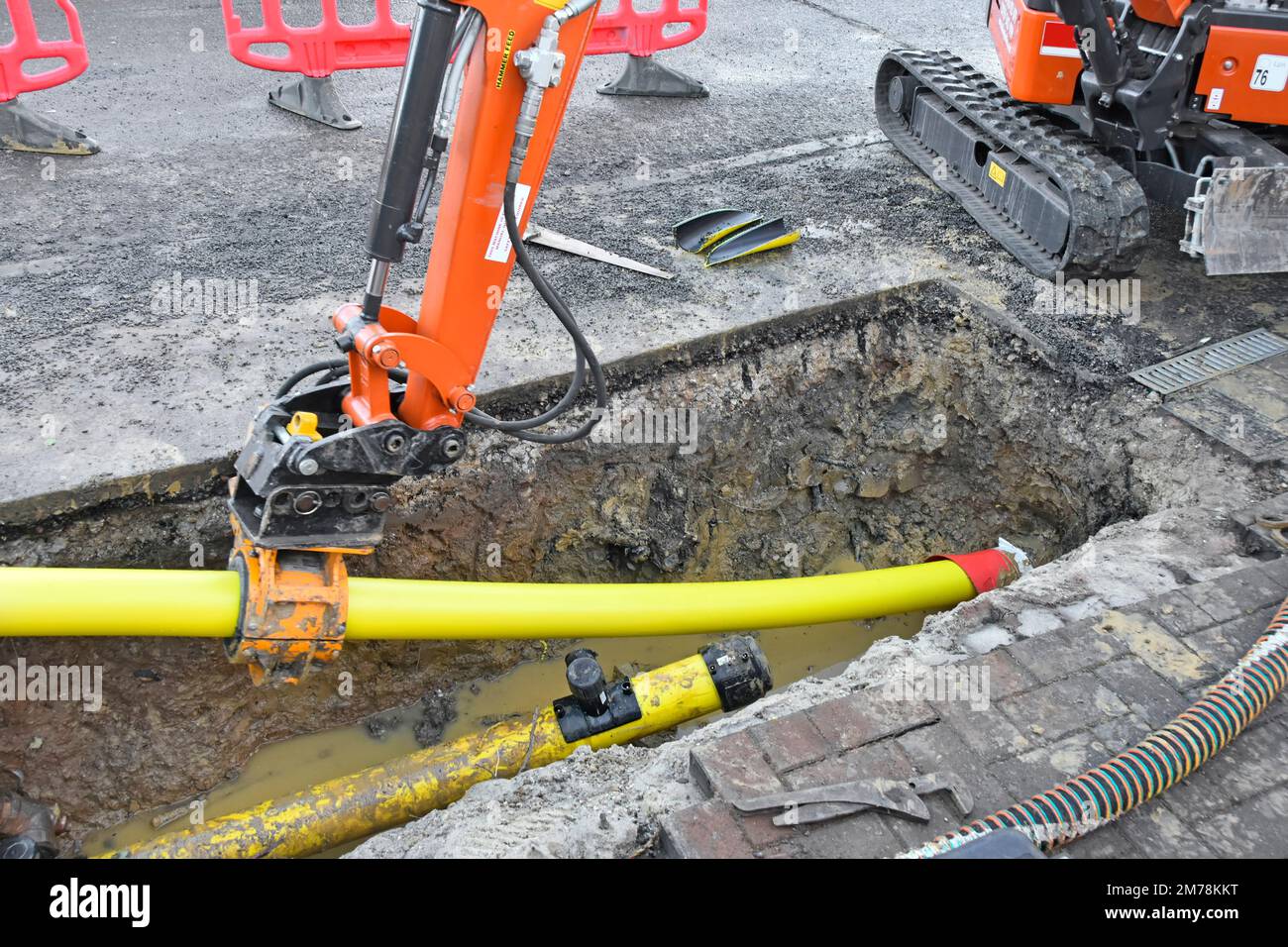 Mini digger hydraulic clamp fitted to back actor arm gripping 125mm replacement yellow plastic gas main pipe pushed & pulled into old steel pipe UK Stock Photo