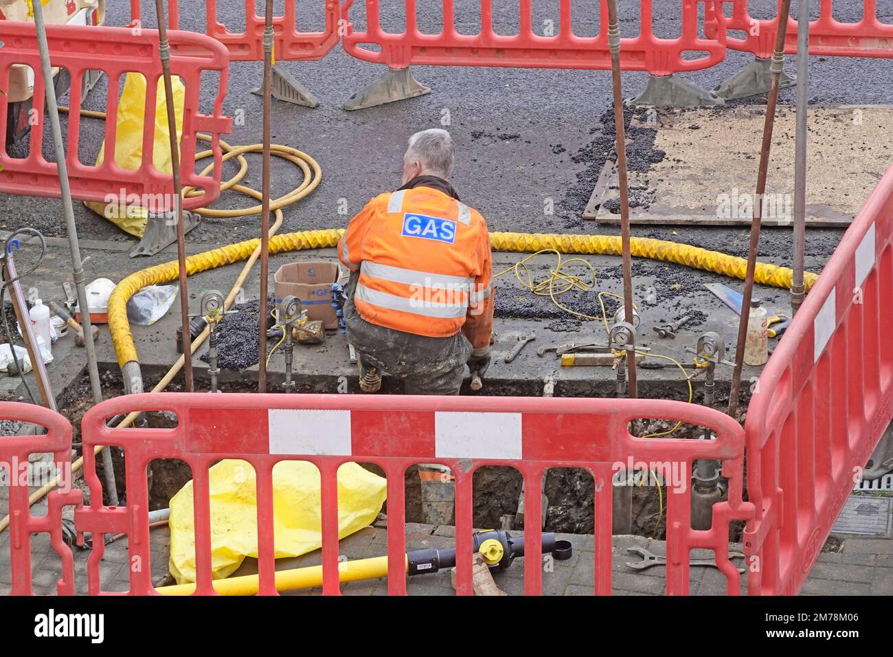 Gas contractor engineer standing in wet pavement pit trench monitoring gas pressure & safe 'venting to air' connecting replaced gas mains to UK homes Stock Photo