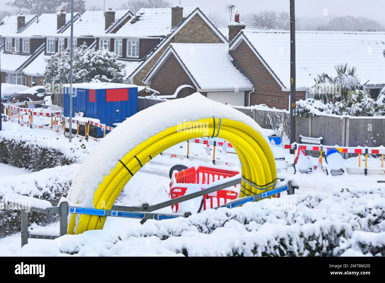 December snowfall & ice stop road work on village underground infrastructure replacement project snow on coiled up yellow plastic gas main pipe in UK Stock Photo