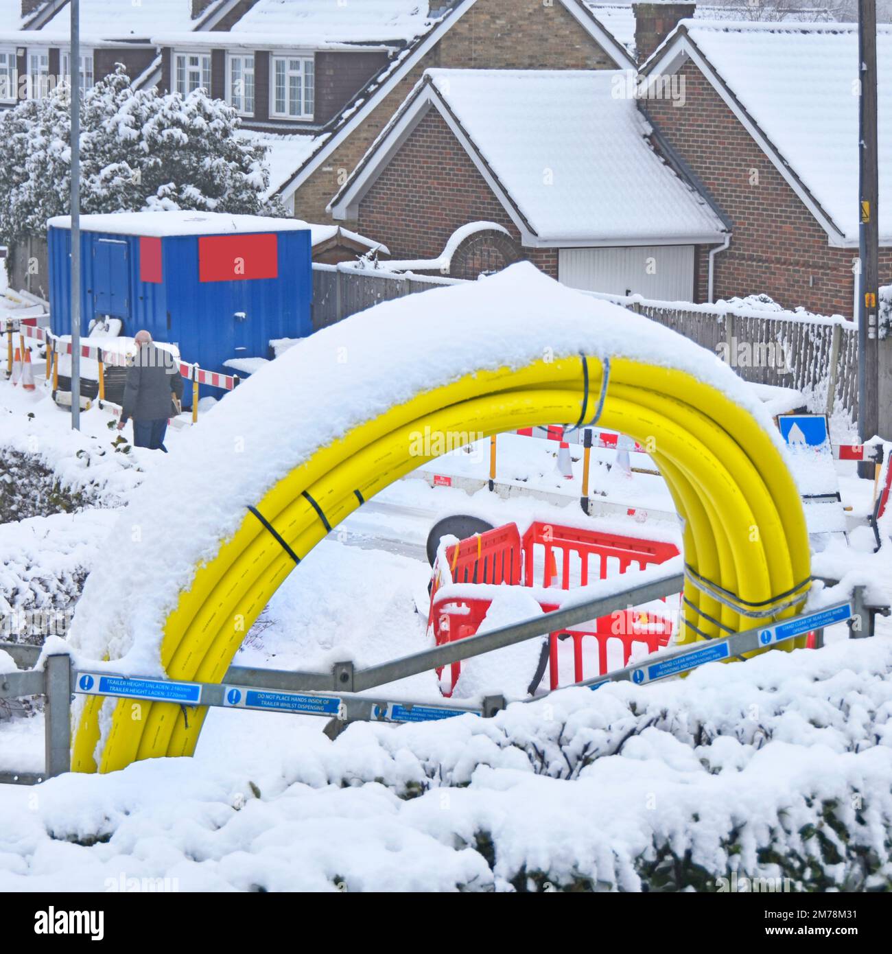 Winter snow stops work & covers yellow coiled up plastic gas main pipe in residential village road works to replace supply to every home in street UK Stock Photo