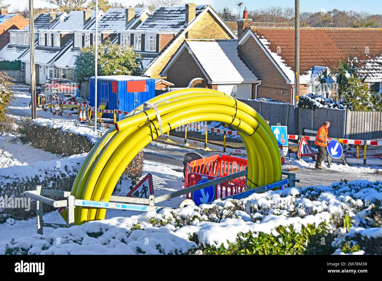 Worker inspects icy snow covered residential village road men stop work on gas main replacement infrastructure unsafe working conditions England UK Stock Photo