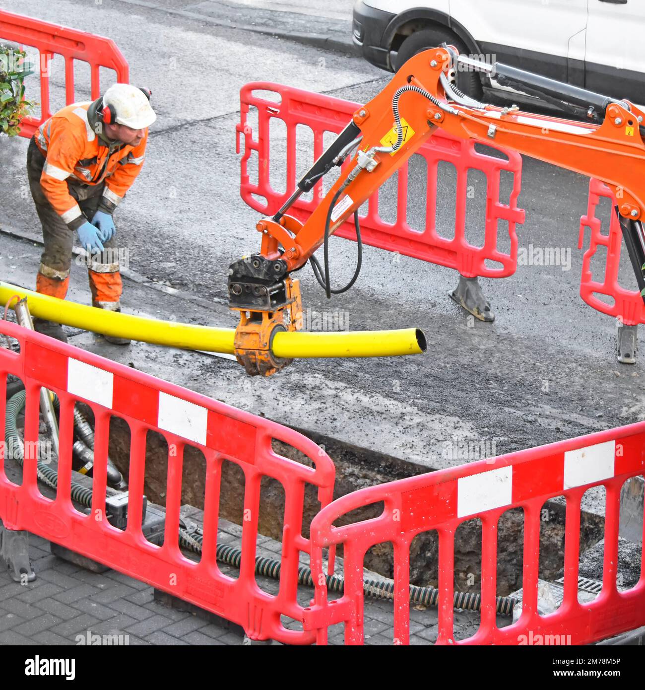 Mini digger hydraulic clamp fitted to back actor arm gripping 125mm new yellow plastic gas main pipe held over pit to be cut to a point England UK Stock Photo