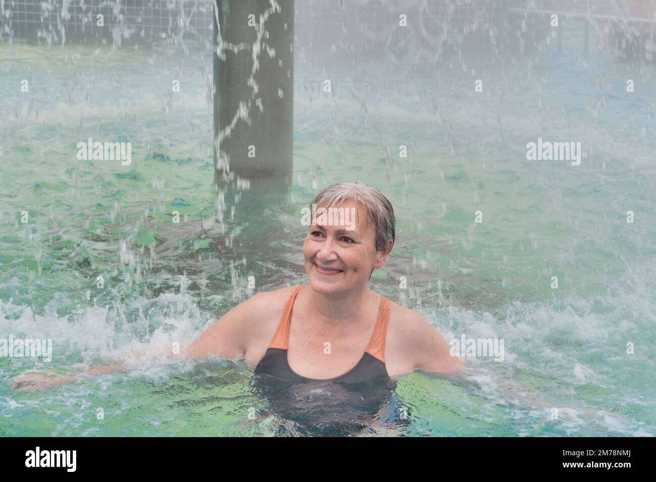 Happy smiling mature woman with short gray hair under jets of water of