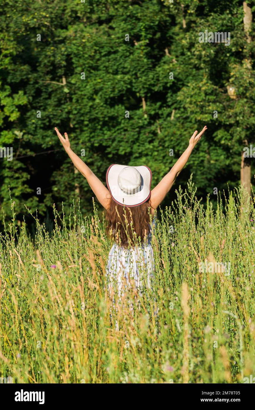 Rear view of happy young woman with long hair in hat and dress pulls ...