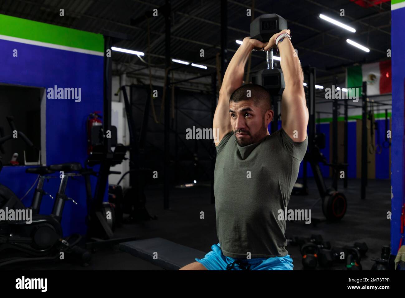 latin athlete doing triceps exercise in a gym with a dumbbell Stock