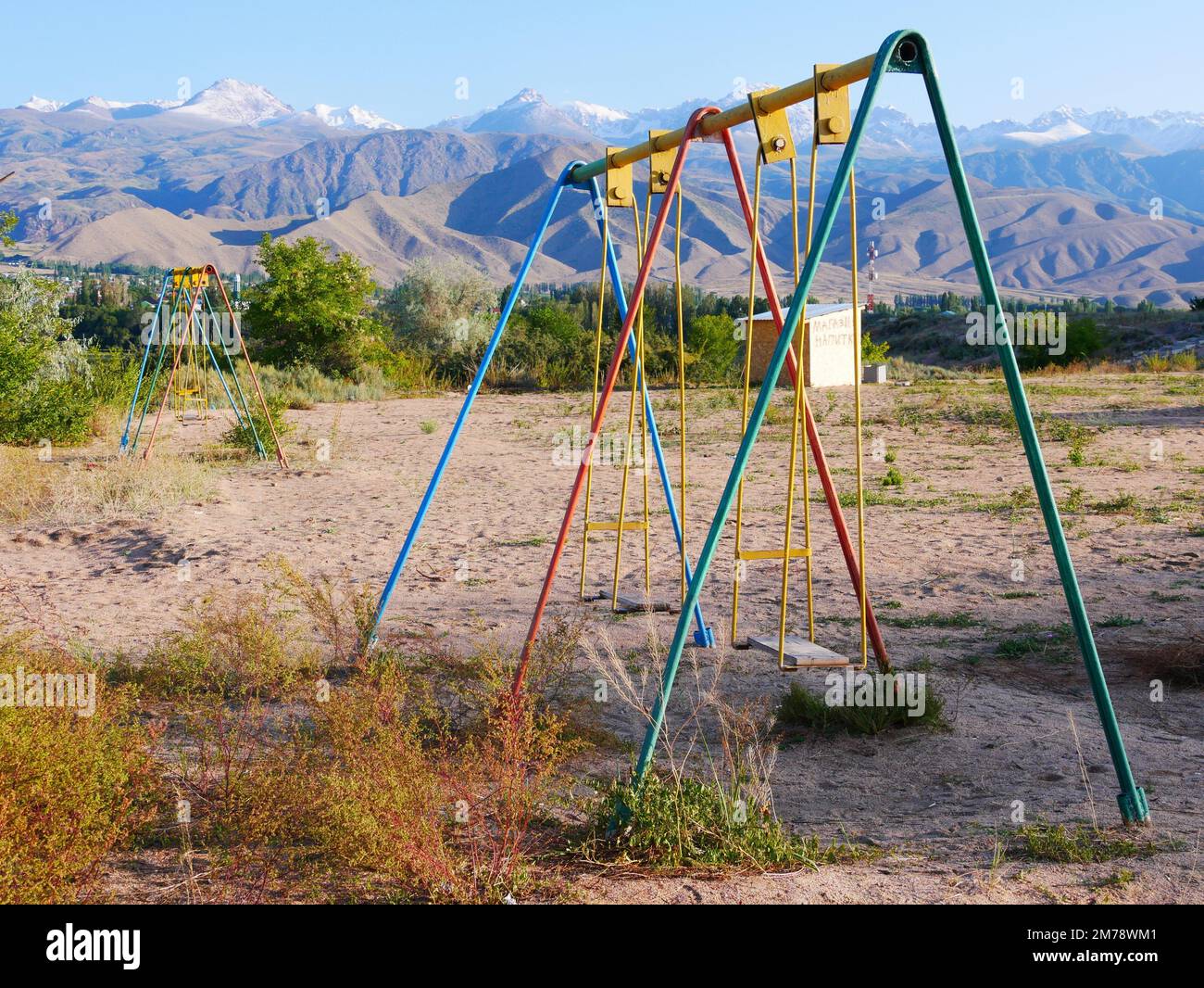 An old metal swingset on a rural field near mountains in Cholpon Ata