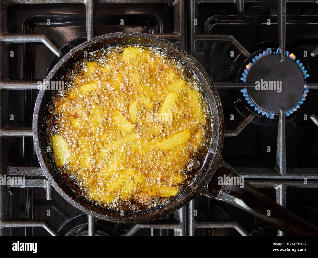 French fries frying in a pan. Fries are deep-fried stick potatoes. Stock Photo