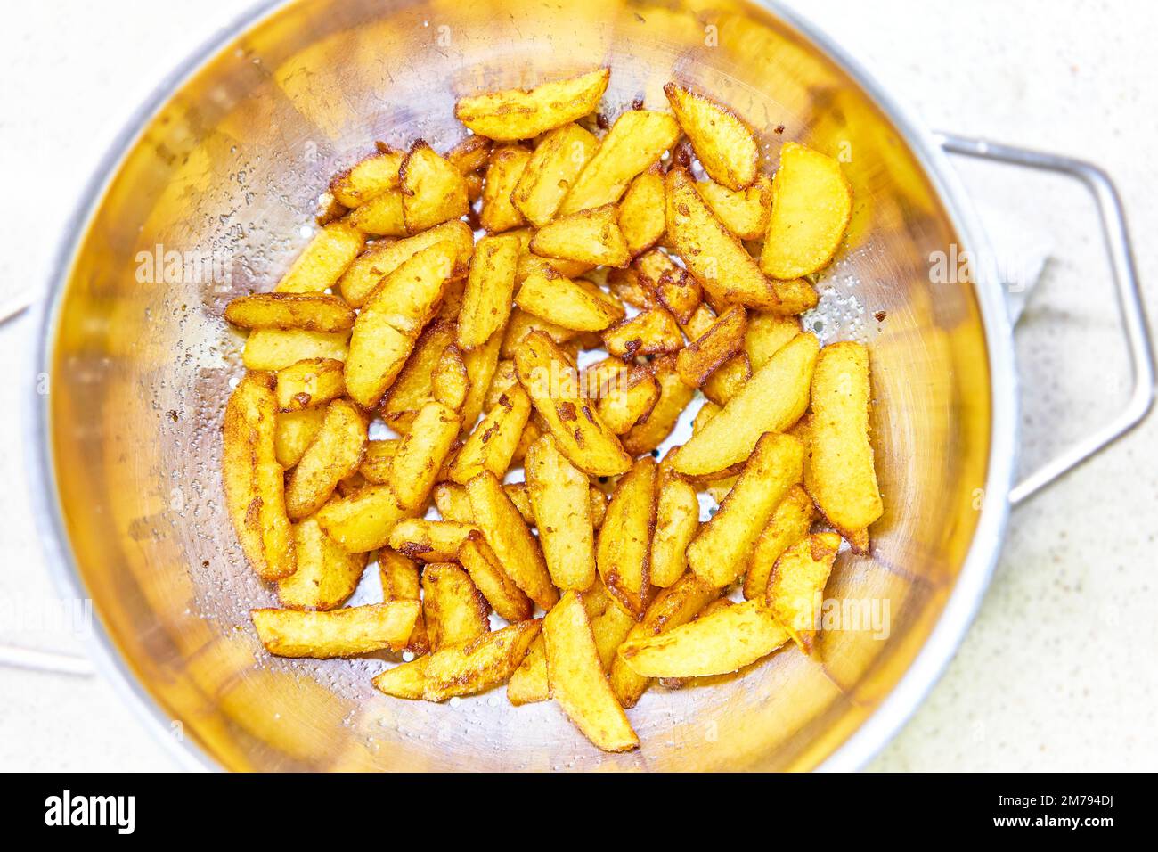 French fries draining the excess fat, after frying, in a sieve. Stock Photo