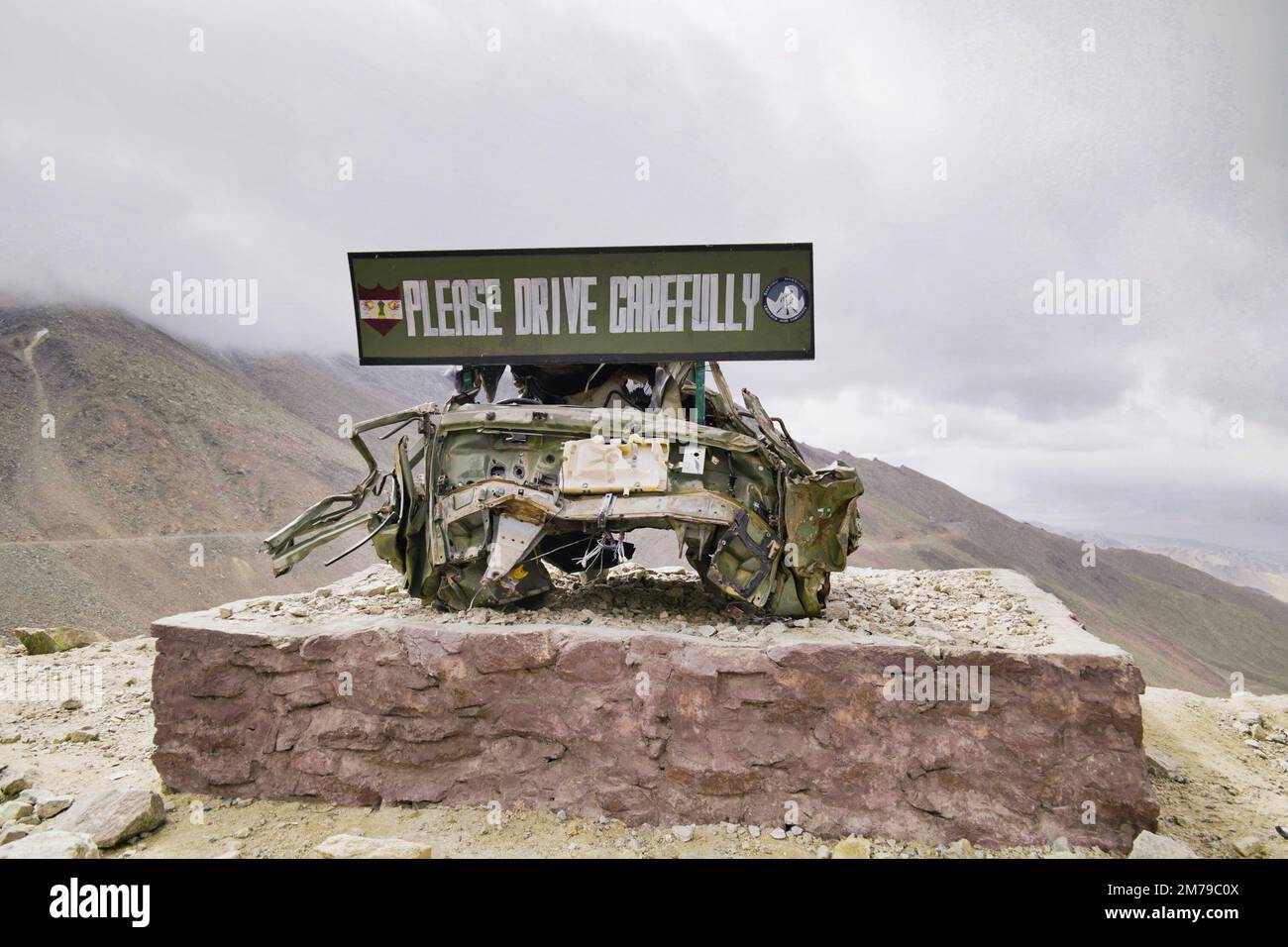 A wrecked car on the Himalayan road with a metallic banner "Please drive samely" on it Stock Photo