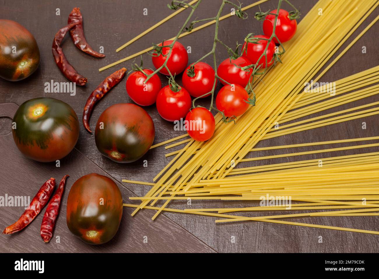 Spaghetti, cherry tomato sprig and whole brown tomatoes. Top view. Brown background. Stock Photo