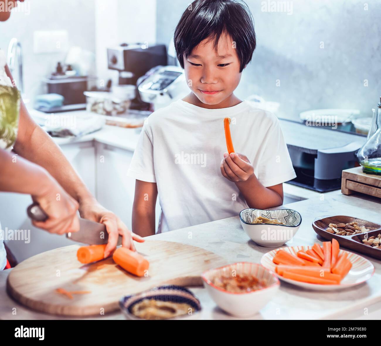 an asian boy cooking with his mother, tasting a carrot. healthy, organic and natural food with the family. Stock Photo