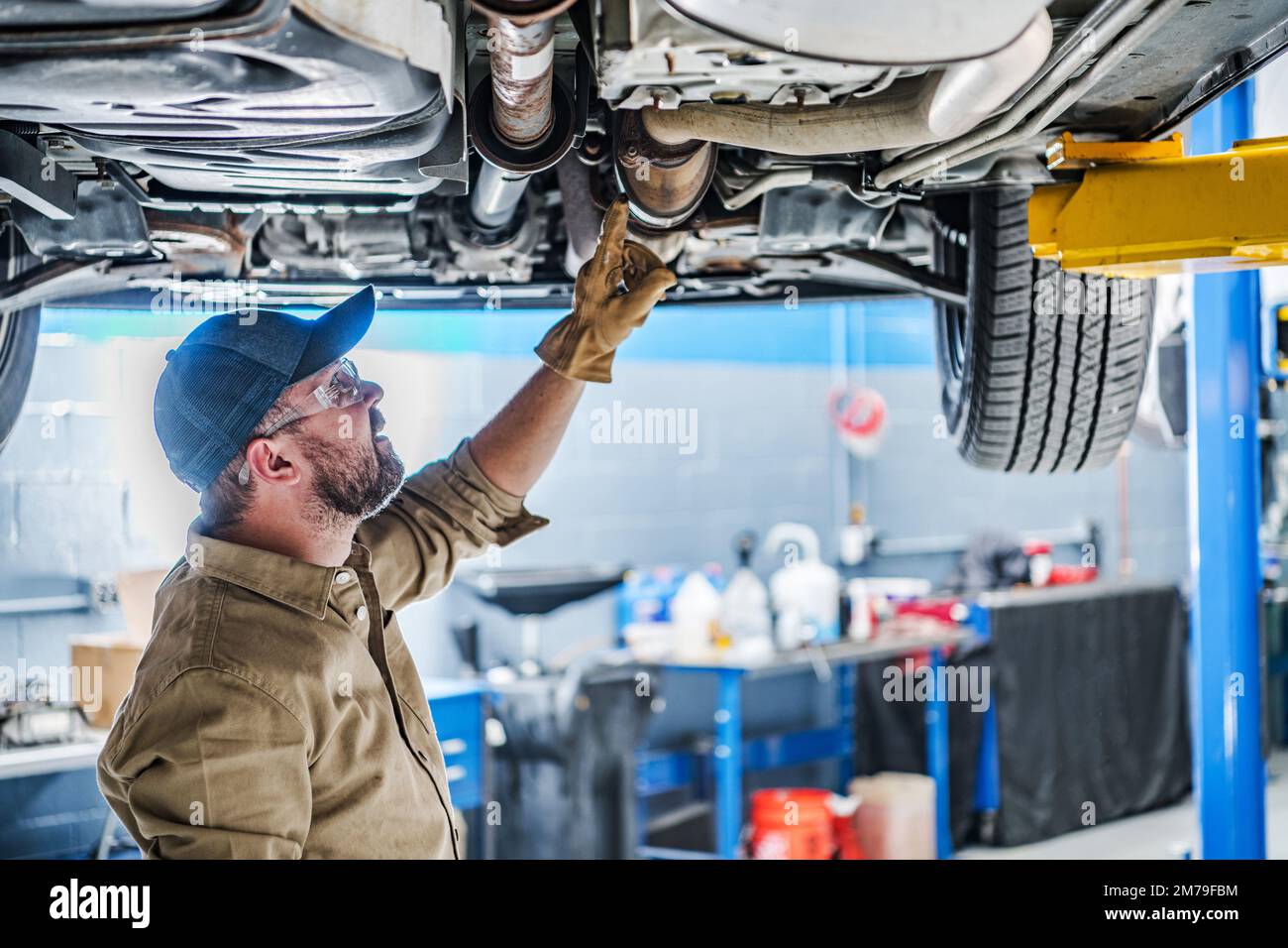 Professional Caucasian Mechanic Standing Under the Vehicle Lifted on