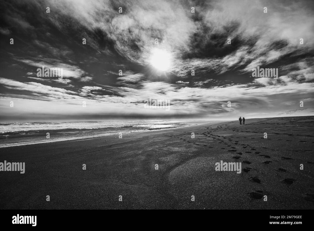 Monochrome image of a couple walking on the black sand beach at Jokulsarlon, Iceland Stock Photo