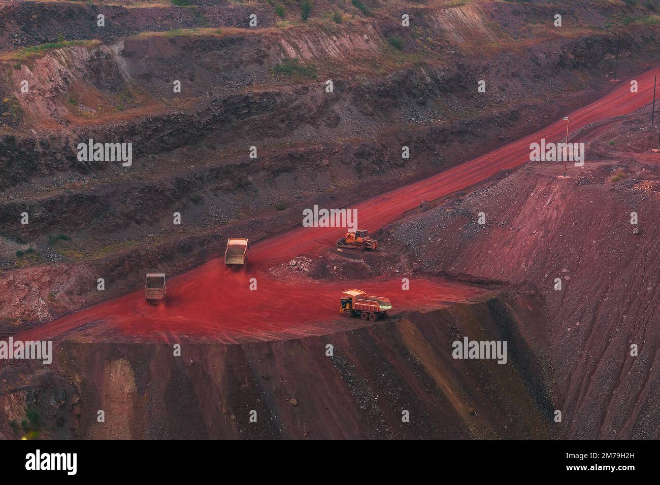 Bulldozer and couple trucks in quarry with red ground. Mining iron ore in Kriviy Rih, Ukraine. Industrial landscape Stock Photo