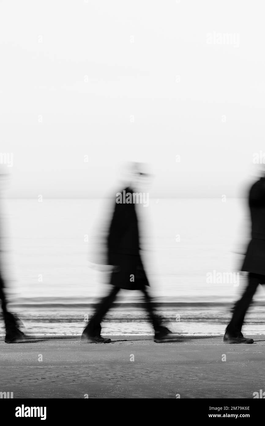 Mysterious man in black suit with glasses walks on the beach near the shore Stock Photo