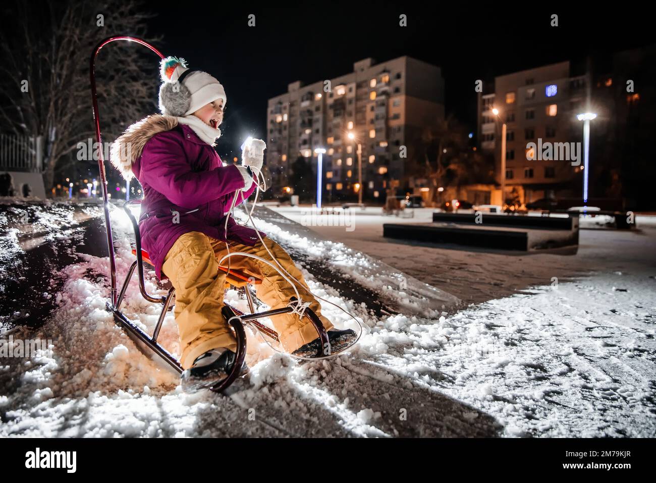 A little girl is sledding on a snowy winter evening. Stock Photo