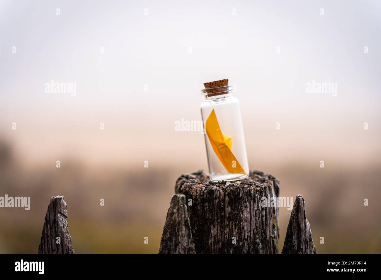 Miniature origami ship in glass bottle standing on a wooden fence at sunrise Stock Photo
