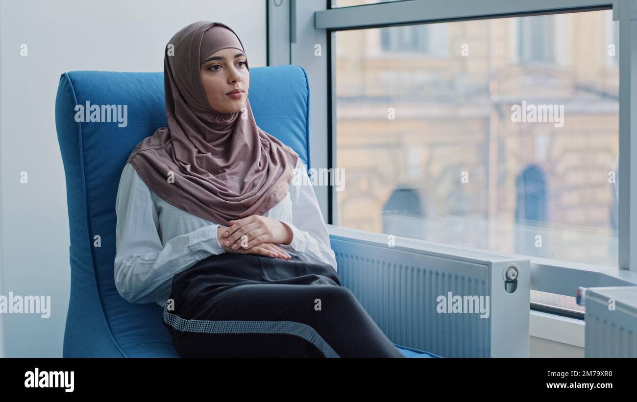 Arabic female Intern student in hijab waiting for exam or interview results in armchair. Job candidate sits at recruit agent office expecting meeting Stock Photo