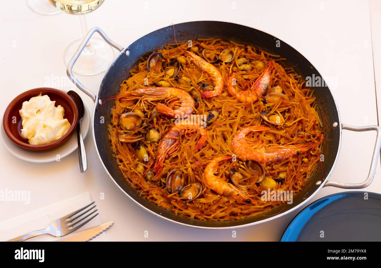 Seafood fideua with shrimps, squid and clams in paellera with allioli Stock Photo