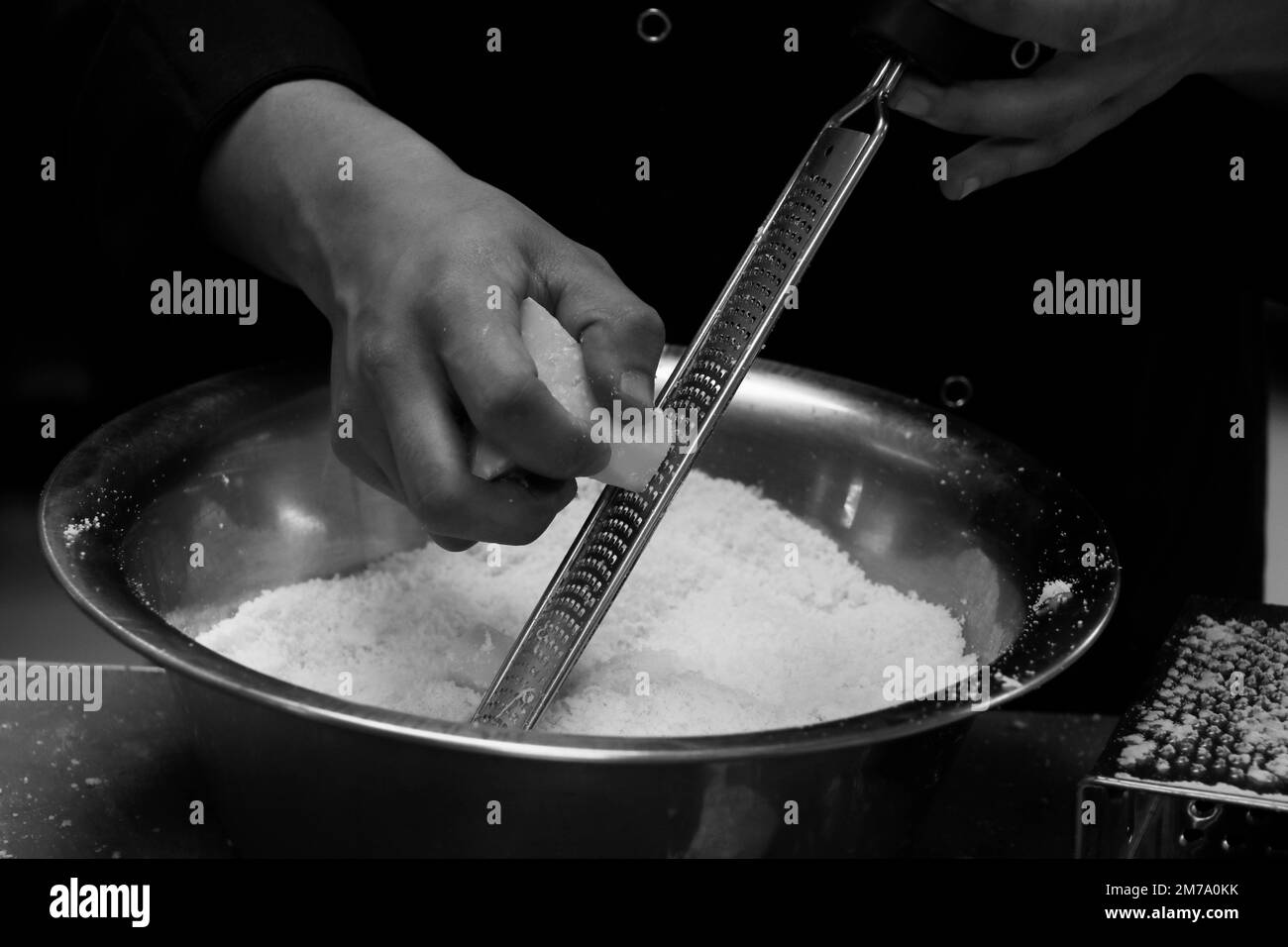 chef grating parmesan cheese with fine grater in close up in kitchen