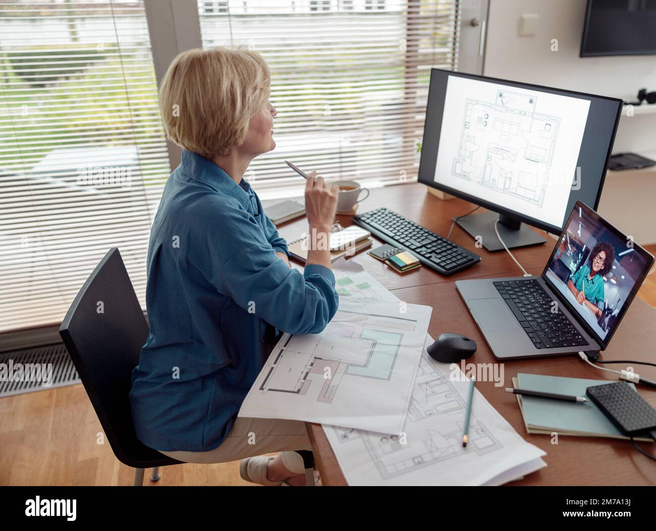 Focused mature woman engineer constructor works on project from home office using computer Stock Photo