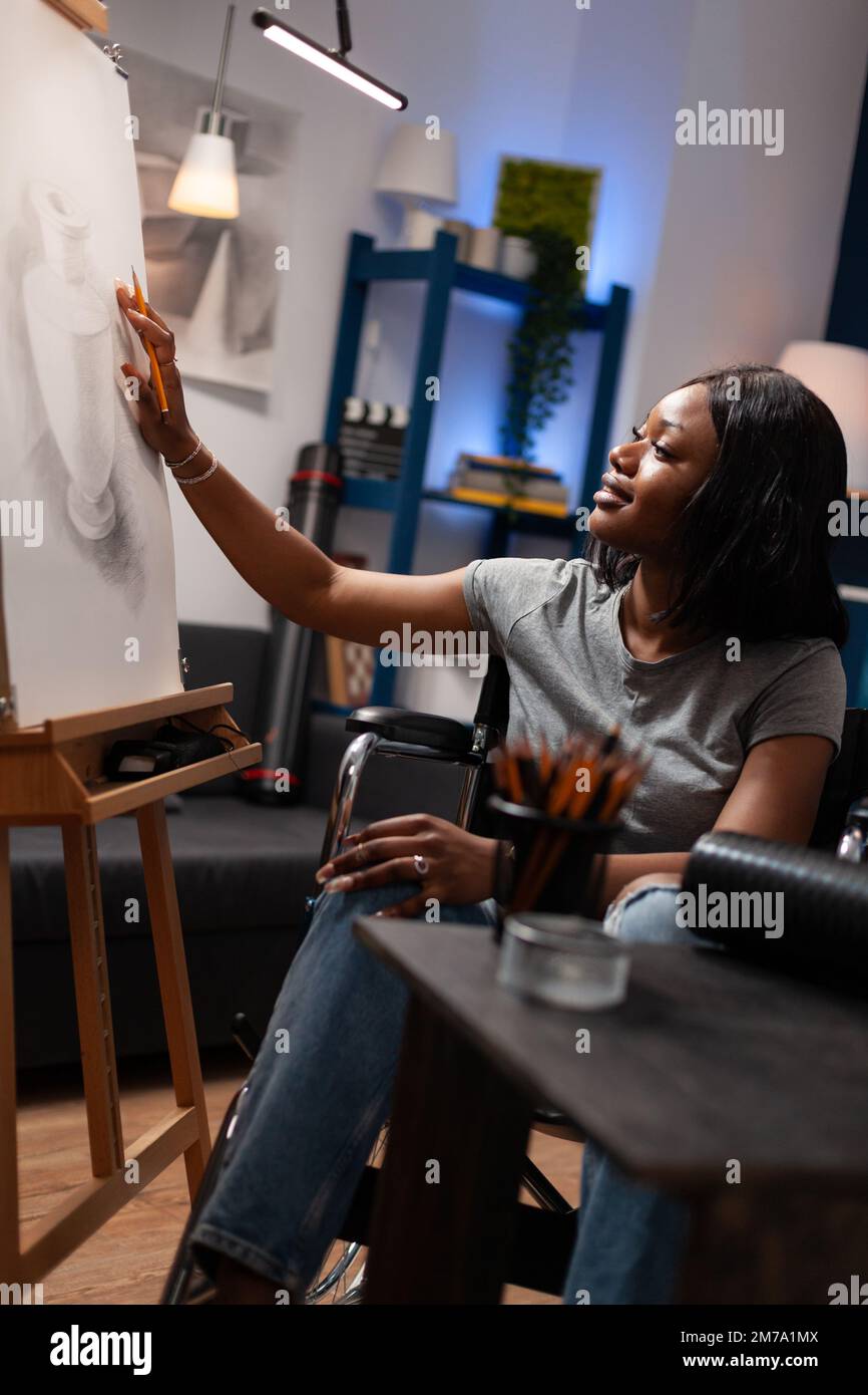 Female art student in wheelchair making pencil sketch on blank canvas in art studio at home