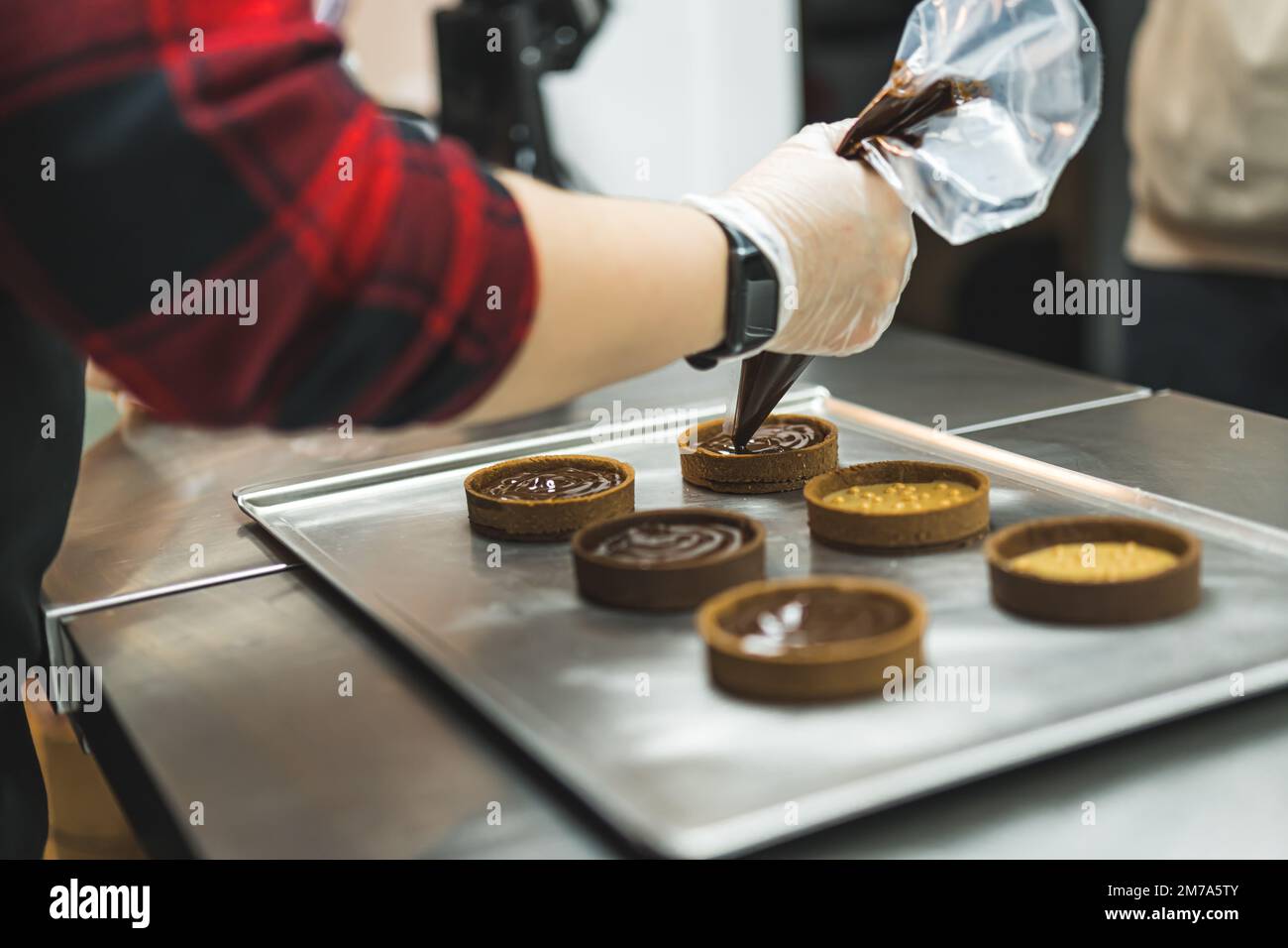Side view of a baker decorating tarts with chocolate icing from a pastry bag. Blurred foreground. High quality photo Stock Photo