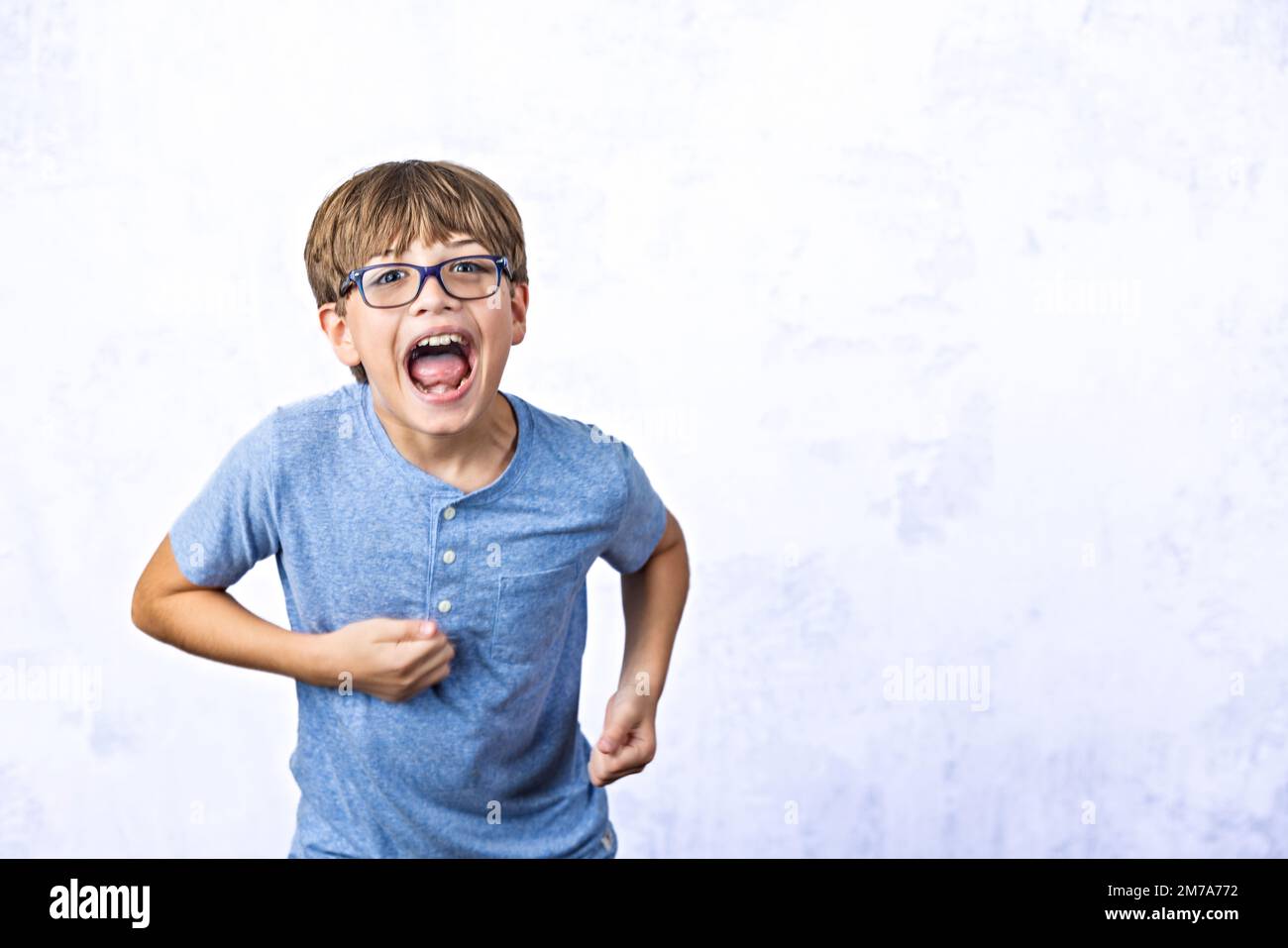 A pre-teen tween boy with glasses with his mouth open and running away on a white background with copy space Stock Photo