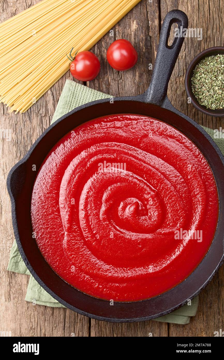 Tomato paste in cast iron skillet, with dry spaghetti, cherry tomato and dried oregano on the